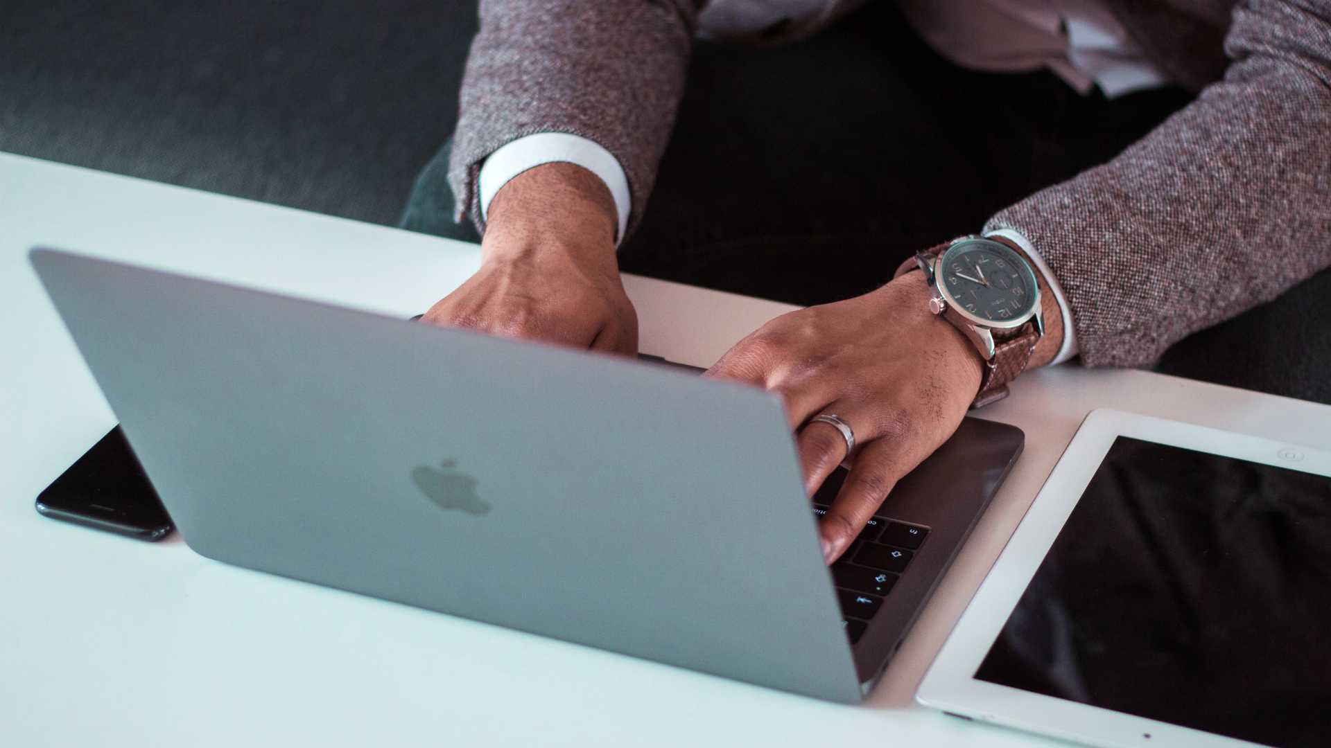Businessman typing on laptop with tablet on desk next to him