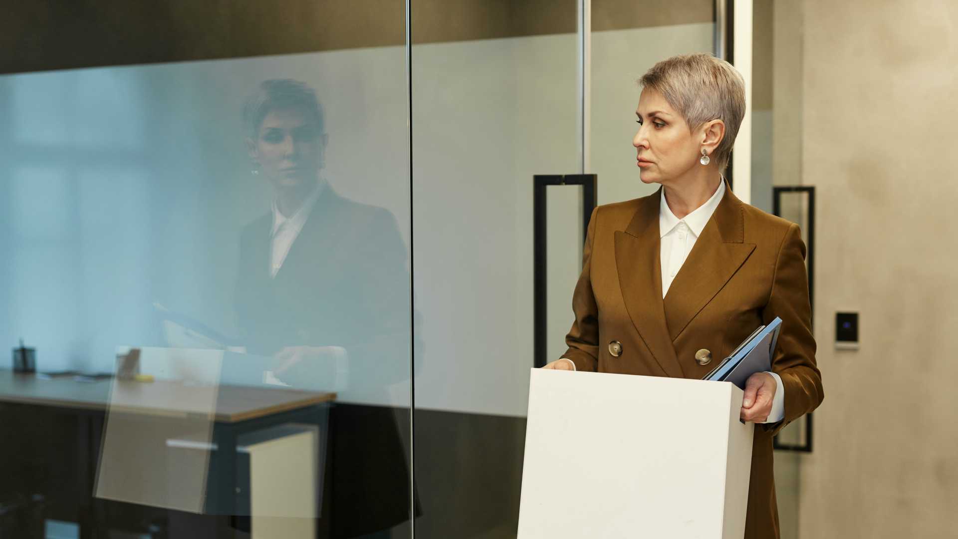 Female executive looking at reflection in glass wall while carrying box of her belongings