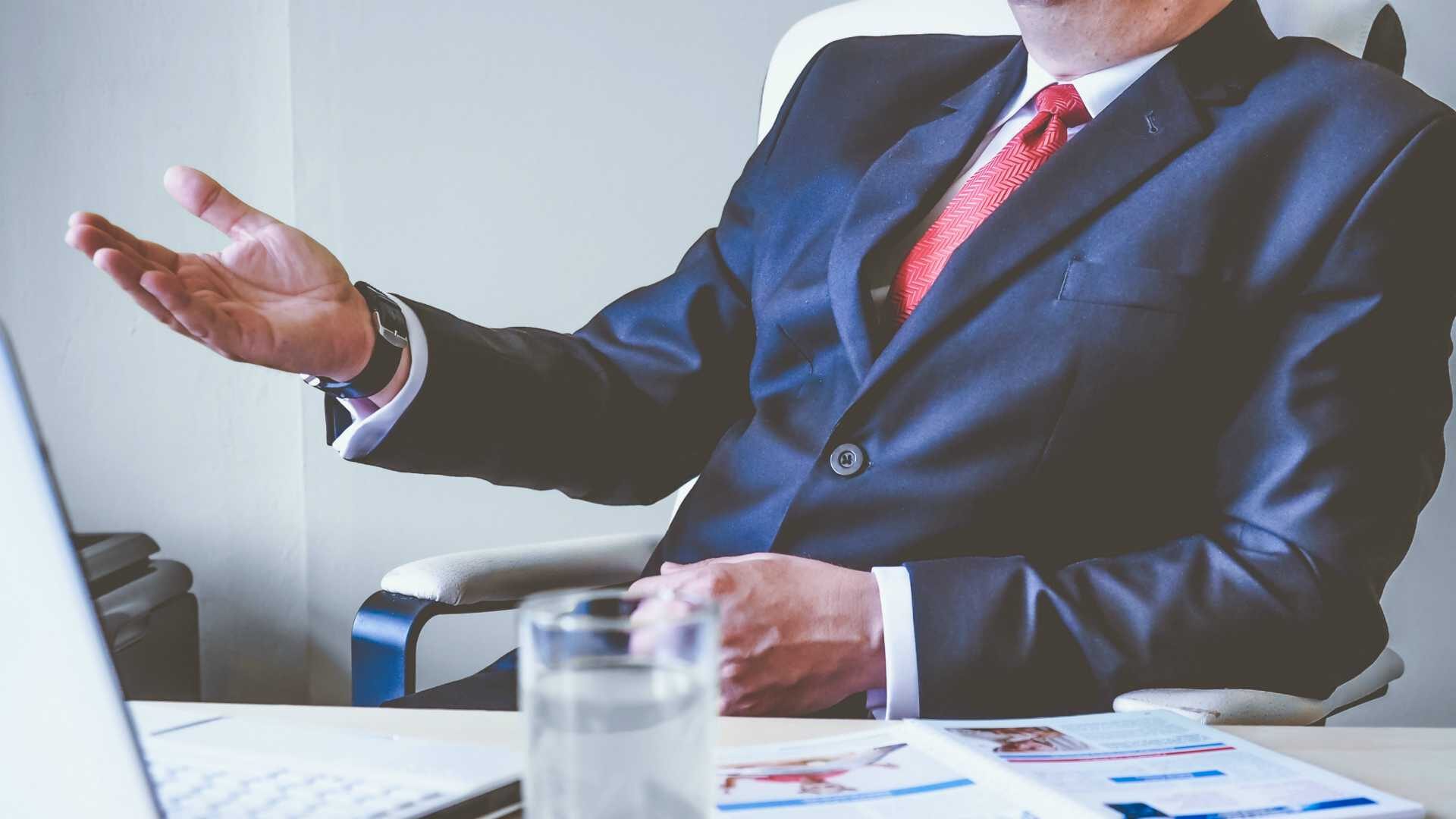 Shot of businessman's torso suit and tie, talking at boardroom table, and gesturing with arm
