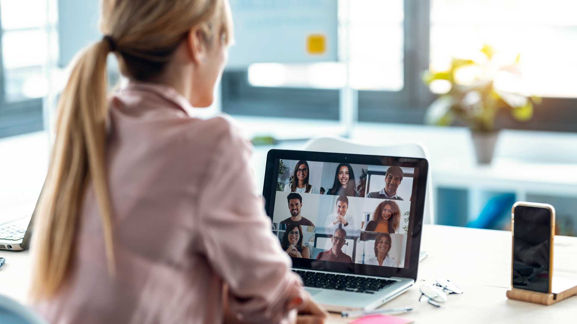 Back view of female employee speaking on video call with diverse colleagues on online briefing with laptop at home.
