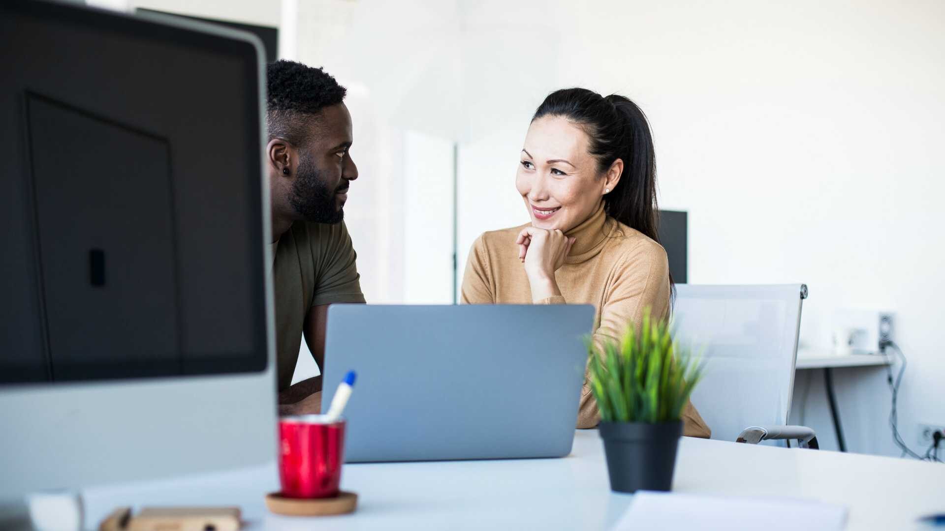 Female leader coaching male employee in while sitting at desk in modern office space