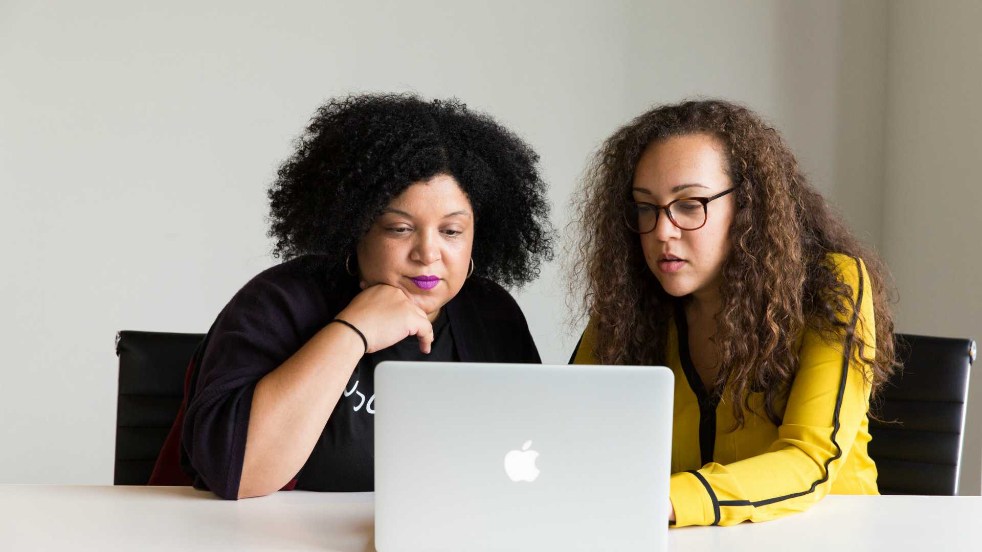 Two racially diverse business women working together on laptop at desk