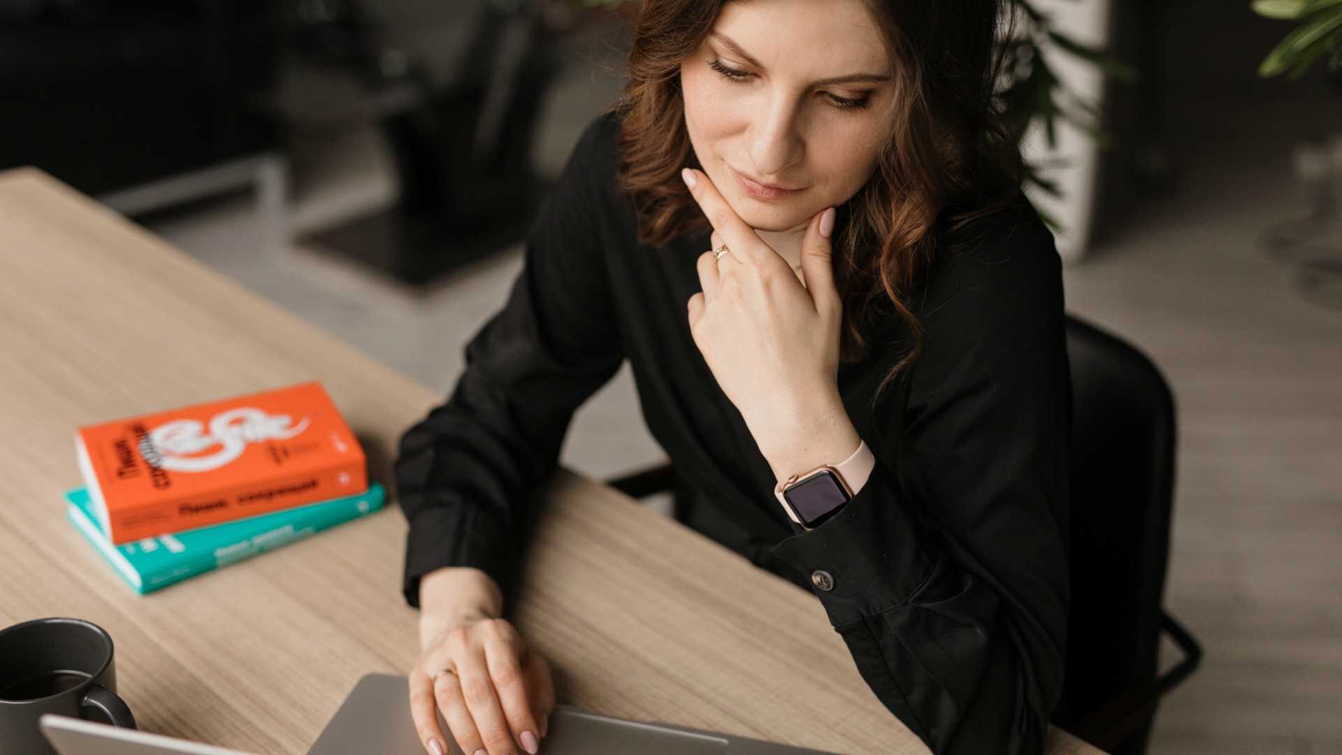 Businesswoman with hand on chin contemplating at desk while working on laptop