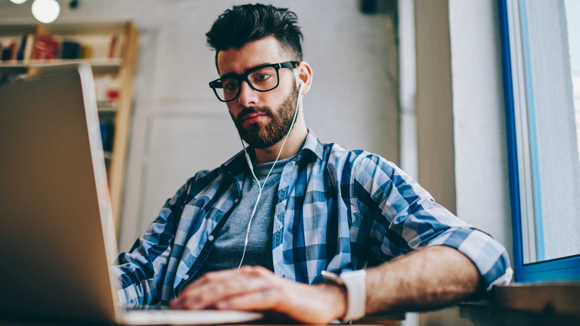 Concentrated male copywriter searching information for new article using modern technology and listening audio book via headphones