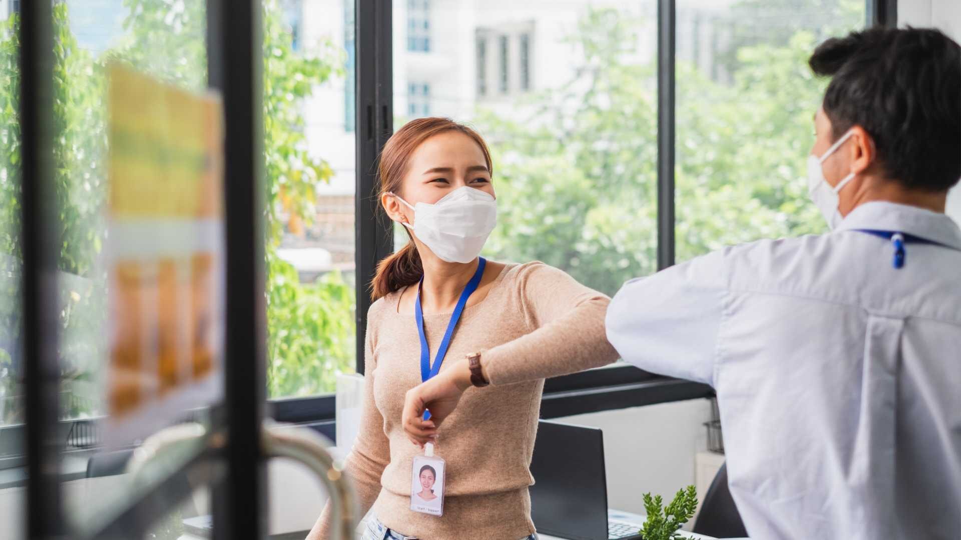 Two business people in masks bump elbows in an office