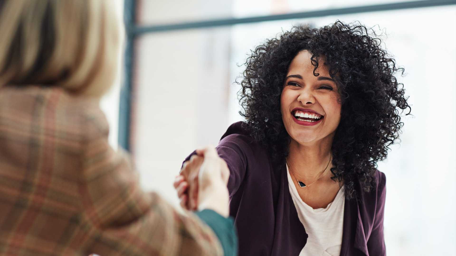 A smiling businesswoman shakes hands with another businesswoman in the foreground