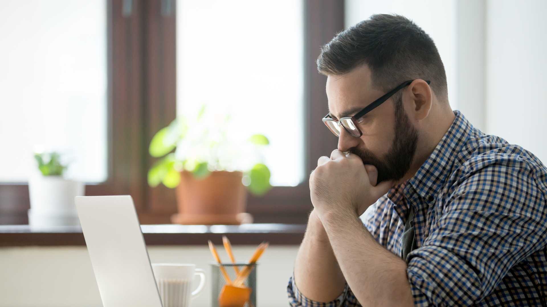 a young bearded professional contemplates his laptop screen