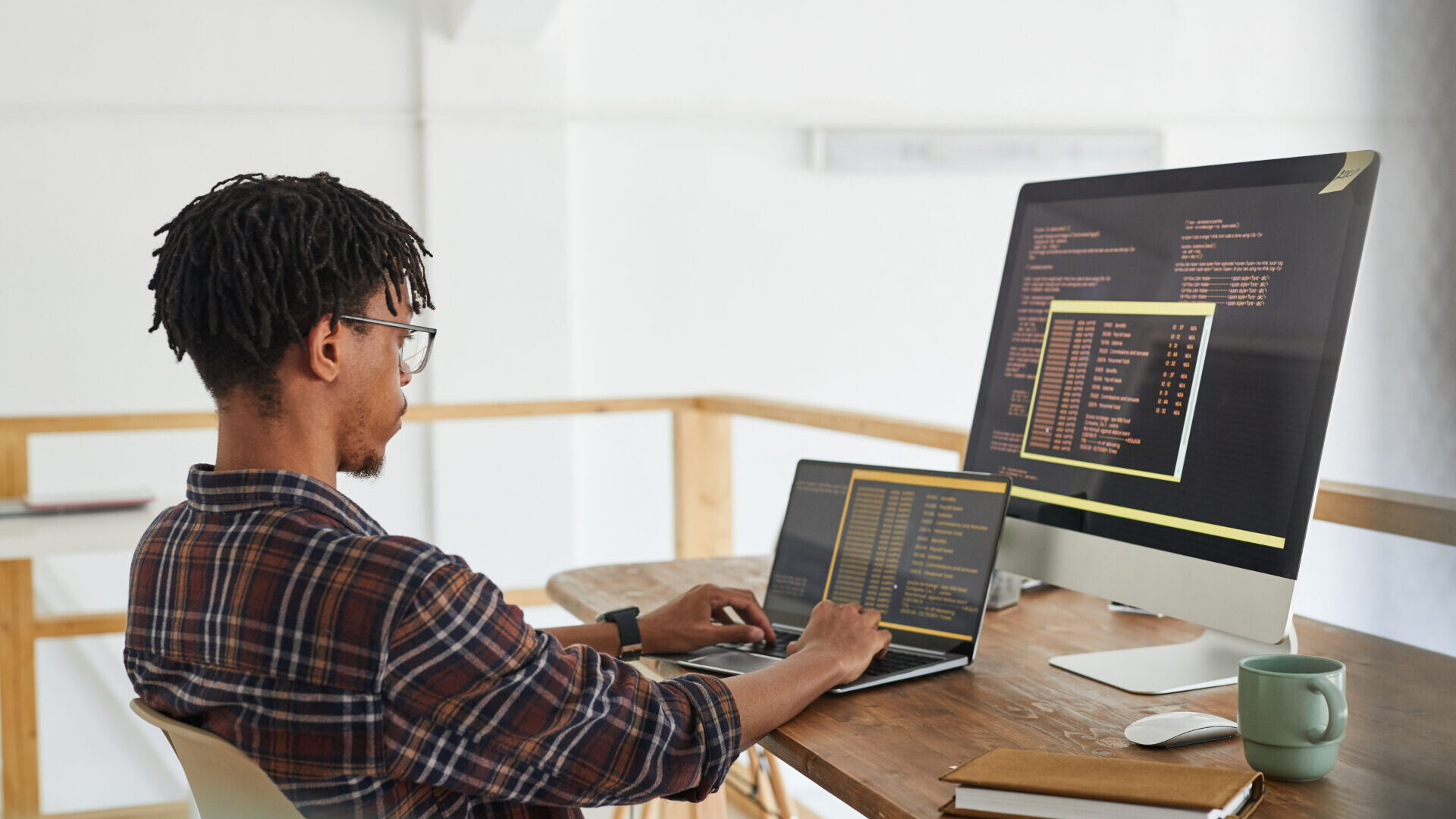 a young Black professional works on two monitors in a home office