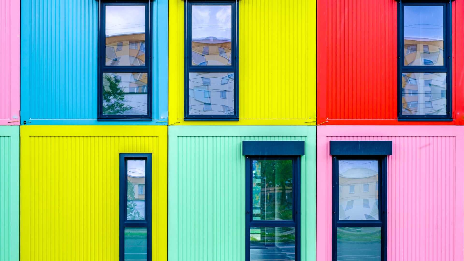 Tiny homes made out of shipping containers are stacked in a row three by two. Each is painted a different, vibrant color.