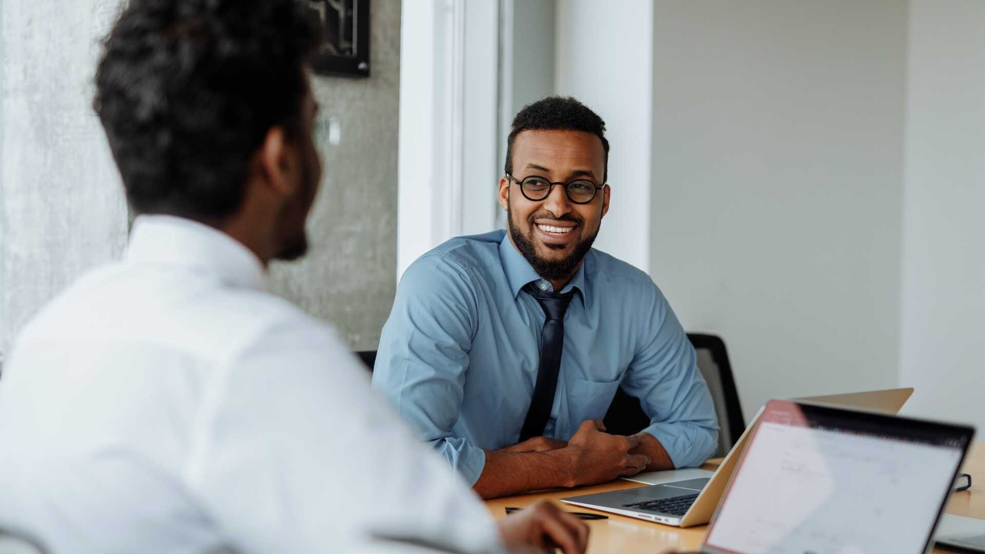 A smiling man speaks with a colleague in a conference room.