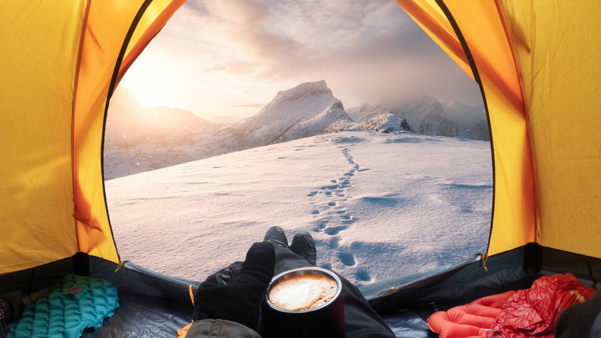 A traveler holds a cup of coffee looking out at footsteps leading up to a snowy mountaintop.
