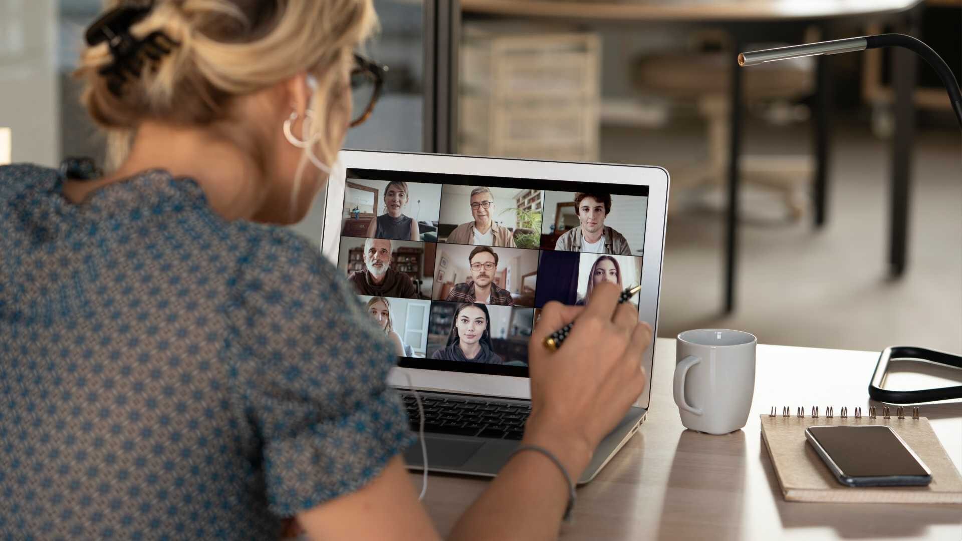 A woman attends a virtual meeting session while sitting at a desk.