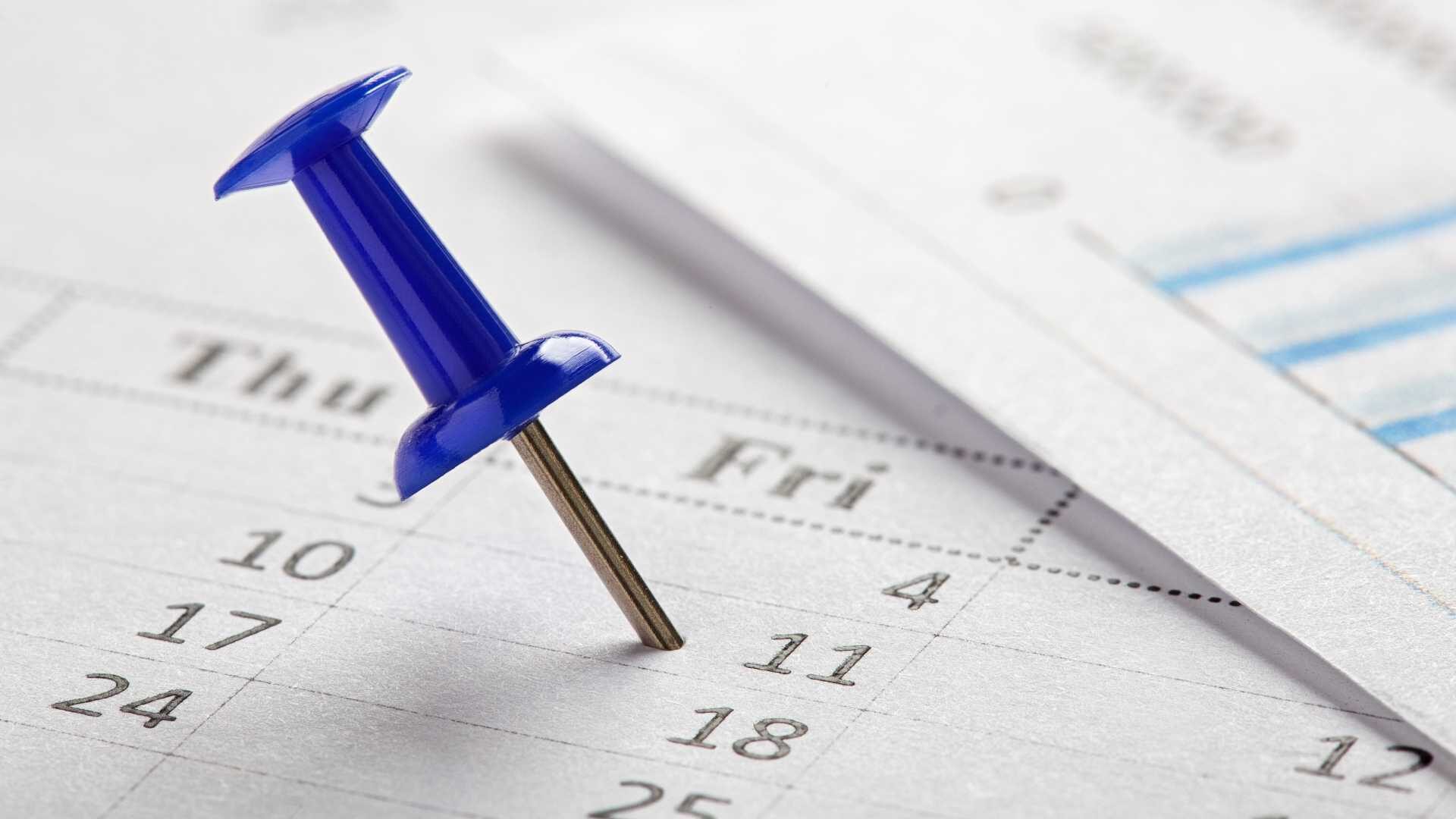 A blue push pin is marking a date on a calendar.