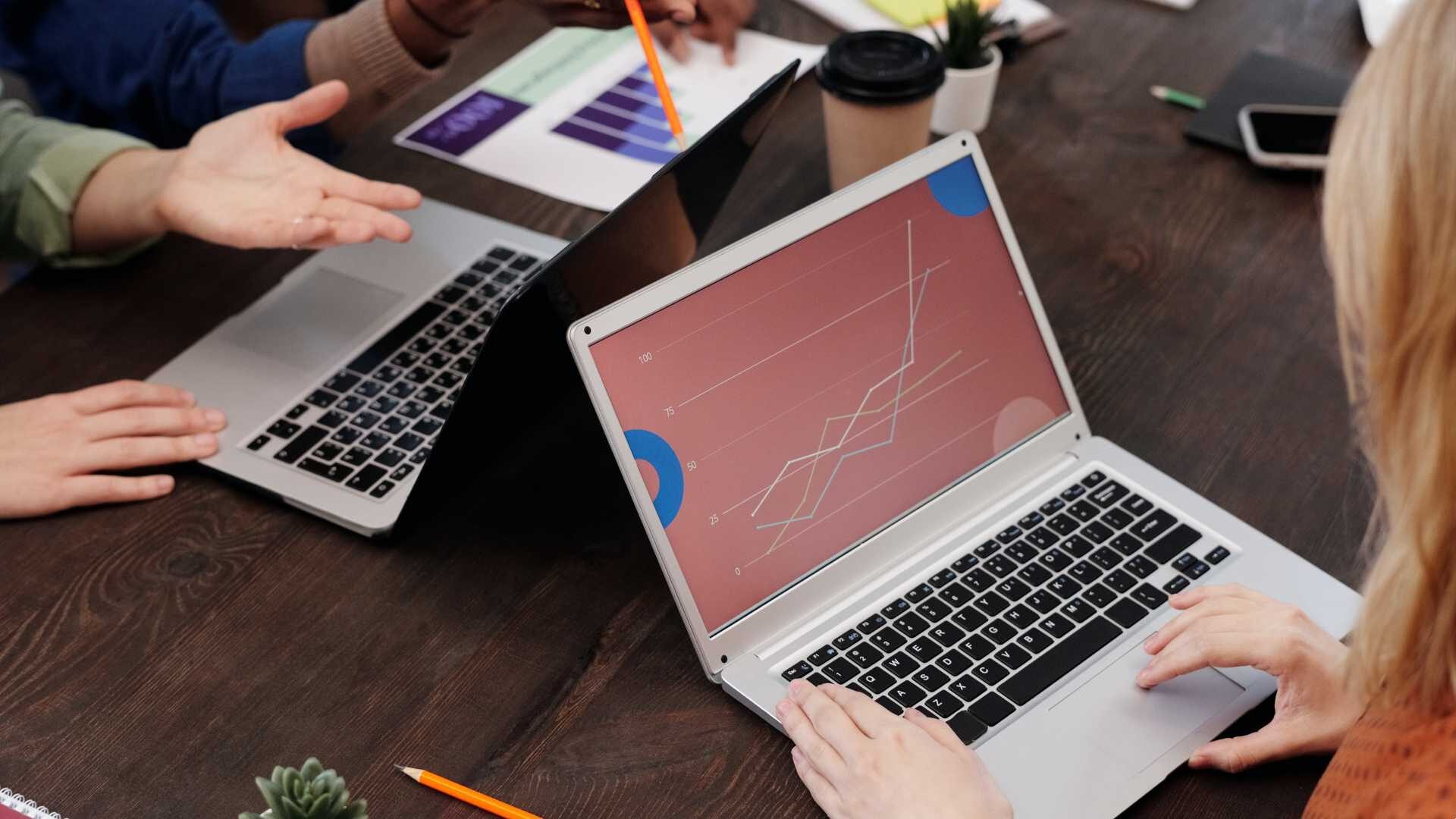 Hands typing on several laptops together on a worktable, strategizing digital transformation.