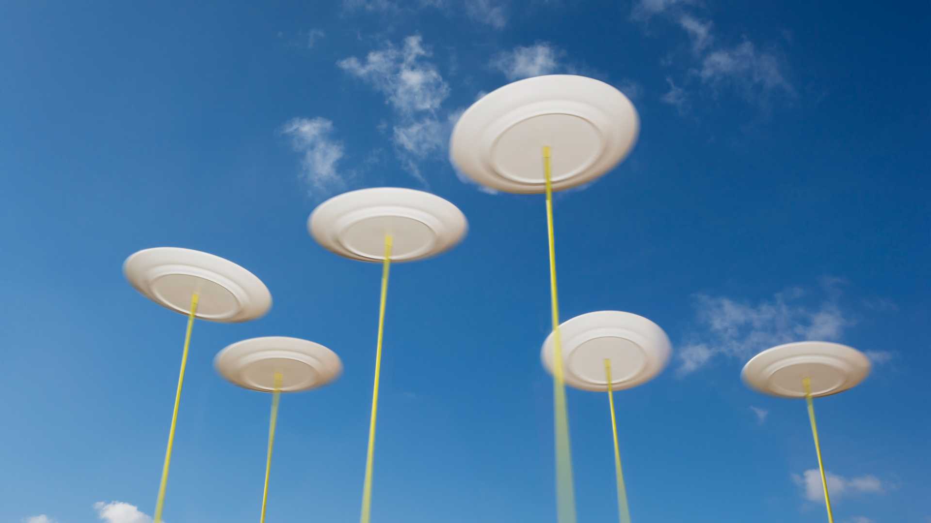 Spinning plates on long sticks pointed to a blue sky with sparse clouds.