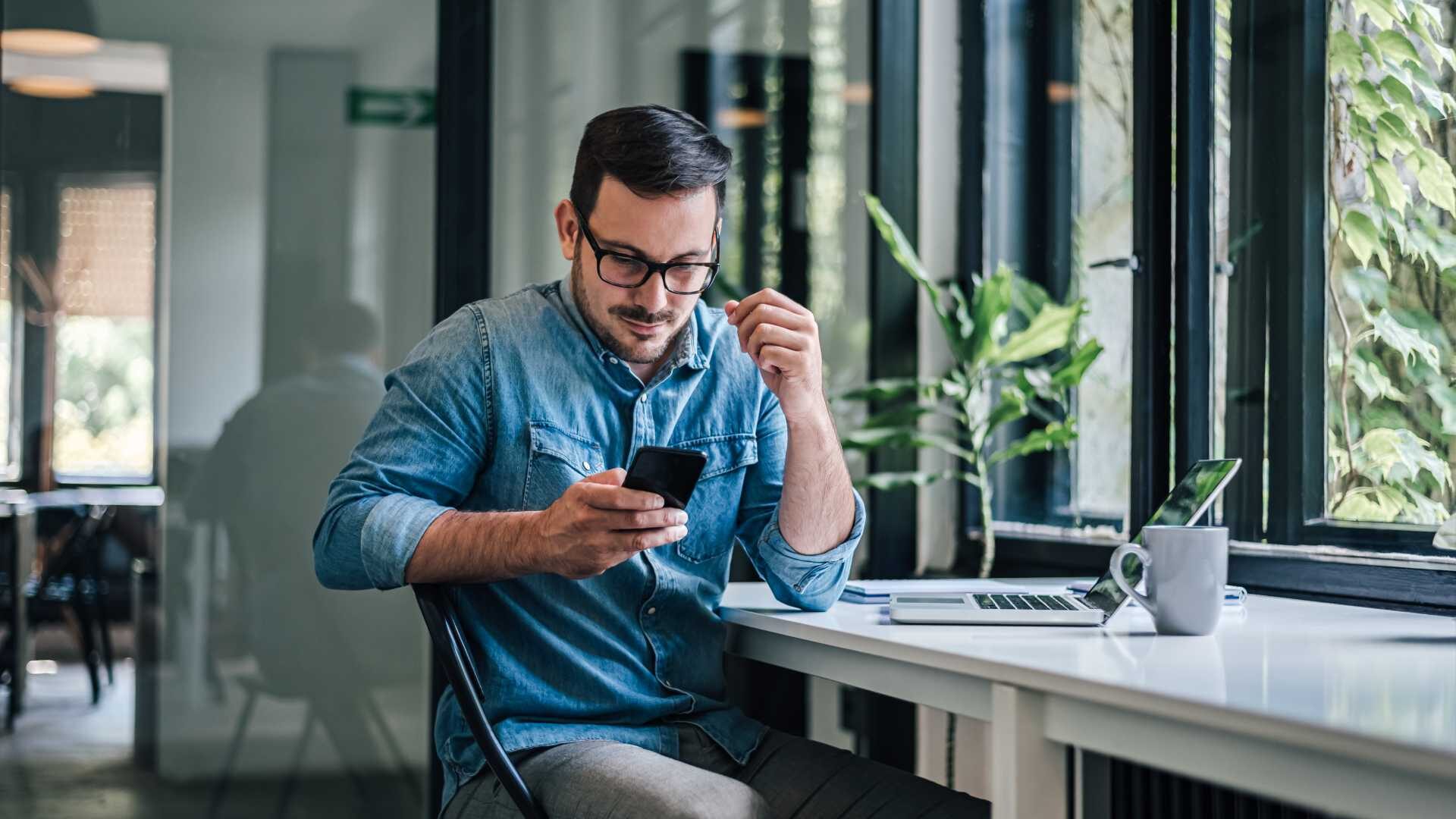 A man working at a countertop in front of a window checks an LMS update on his phone.