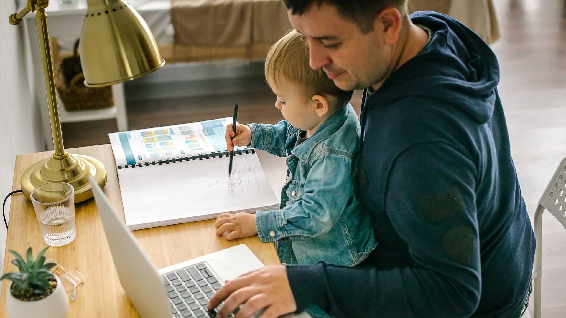 A man holds a child on his lap while working on a computer