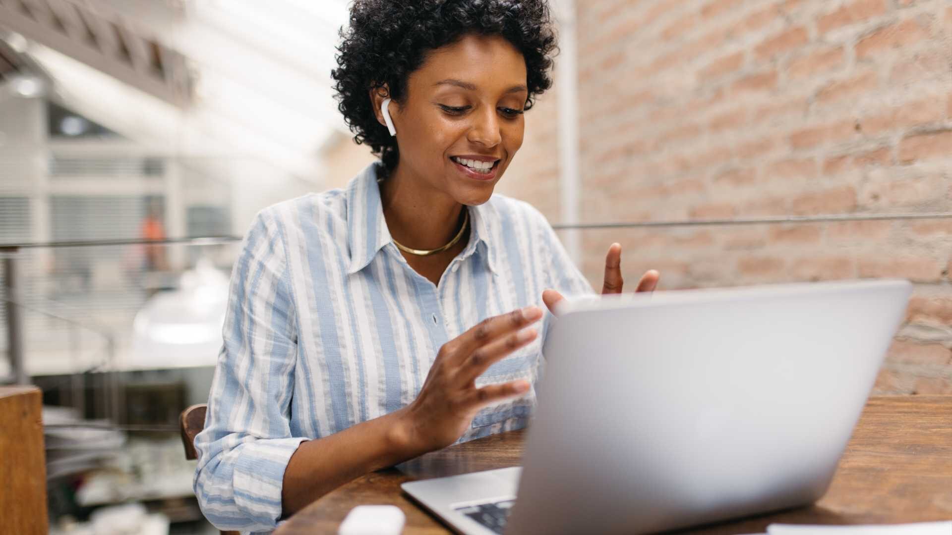 Woman wearing ear pods engaging in a meeting over her laptop.