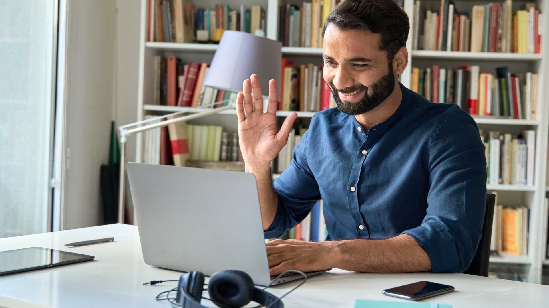 Man sitting at desk on his laptop computer saying hello at the screen.