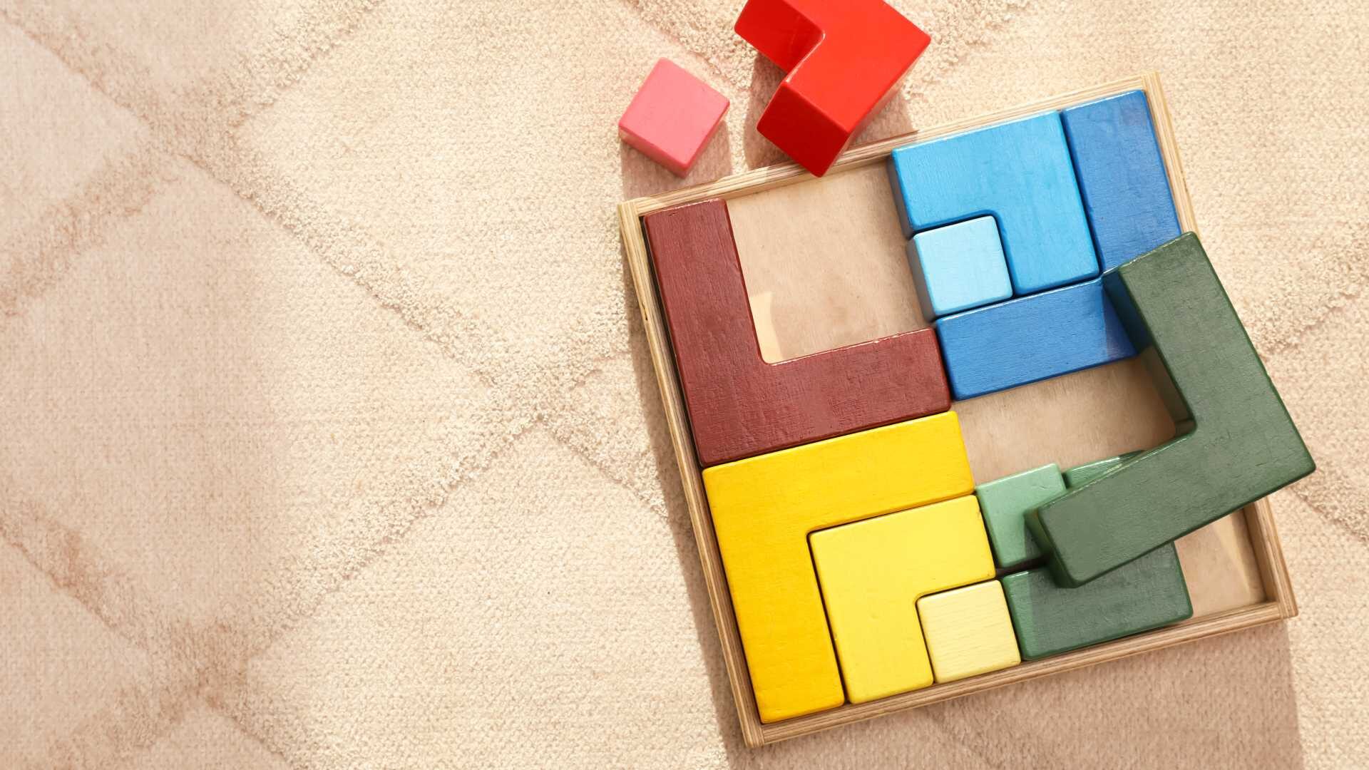 Multi-colored geometrical block puzzle on a diamond-patterned rug.