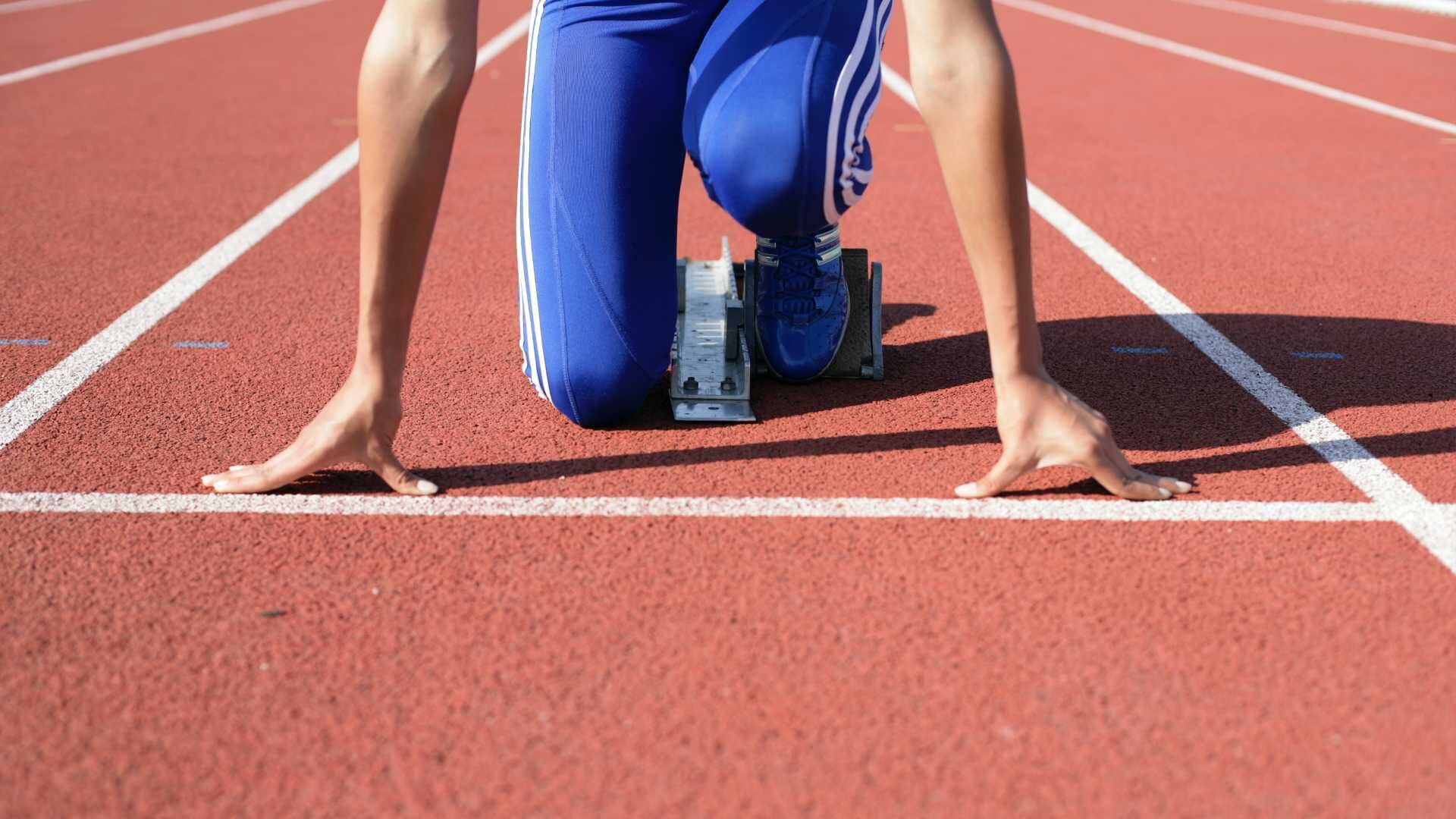 A runner kneels in front of a start line on an outdoor track