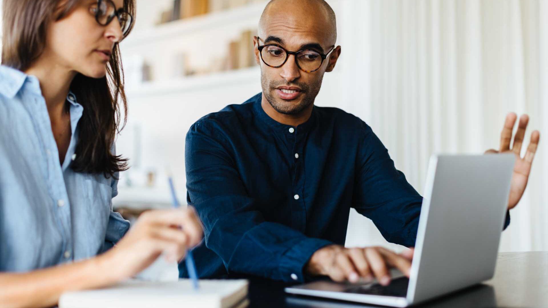 A businessman in front of a laptop explaining something to a woman seated next to him