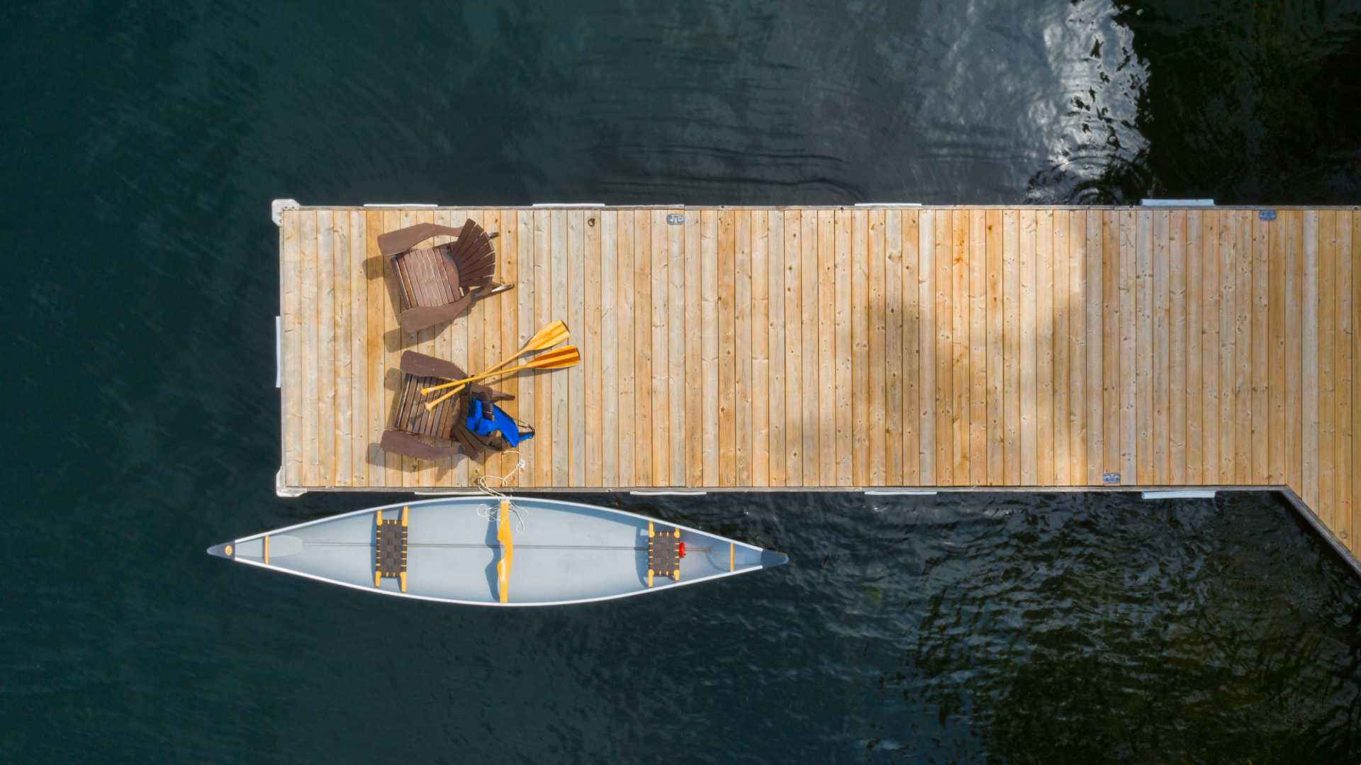 An empty canoe sits next to a dock above dark blue water