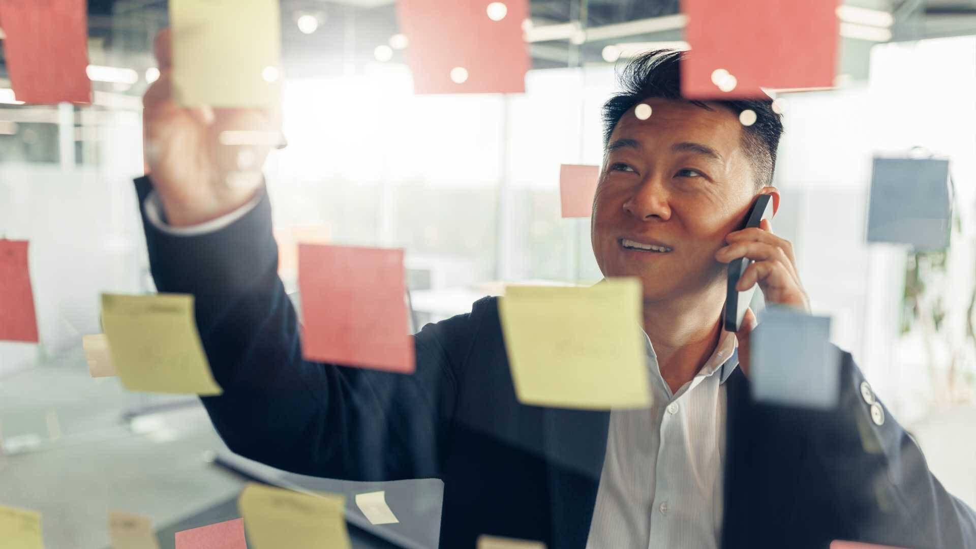 Leader at a company on the phone and standing at a glass board with post-it notes.