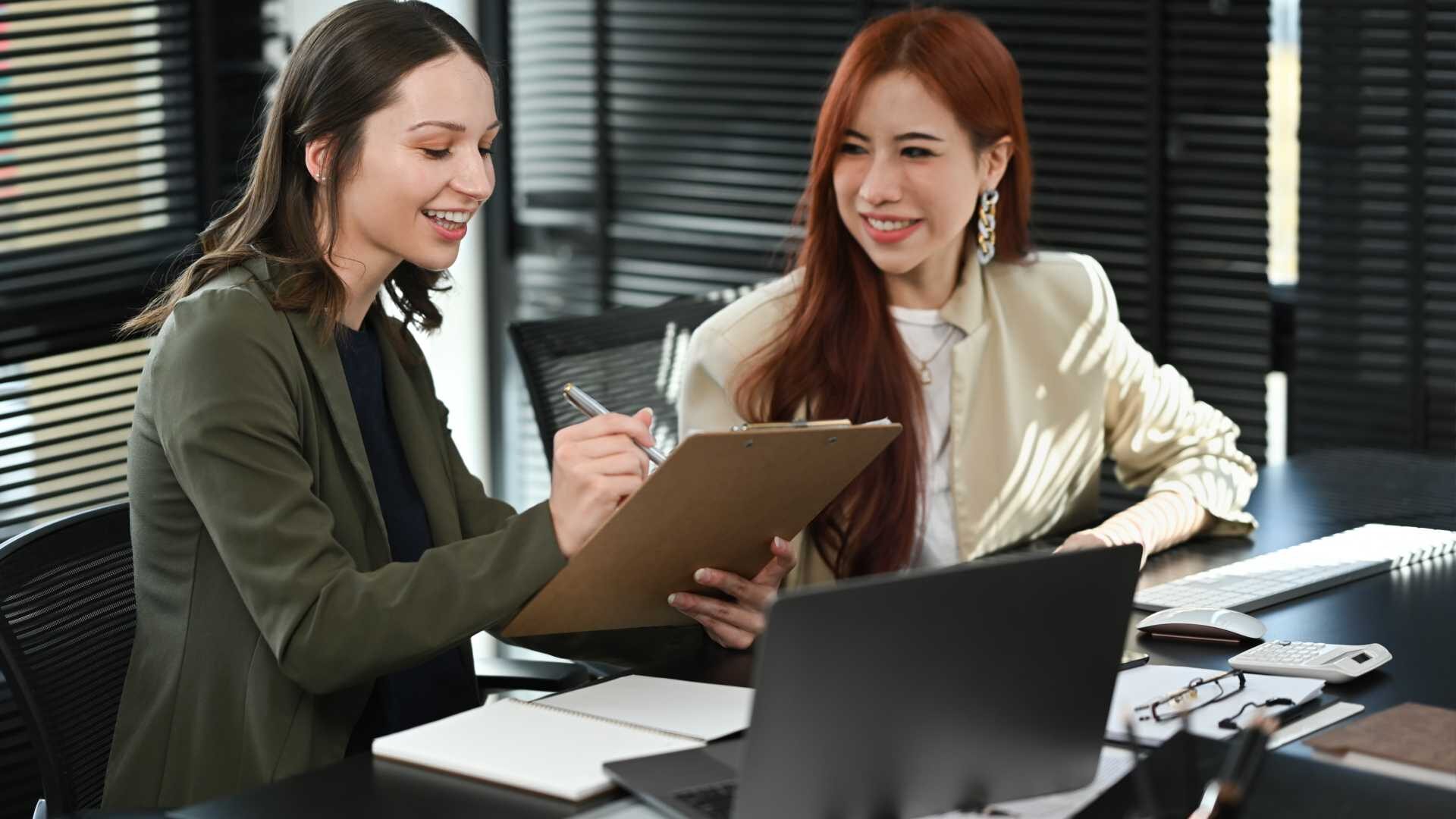 Smiling business colleagues talking and examining financial reports at modern workplace.