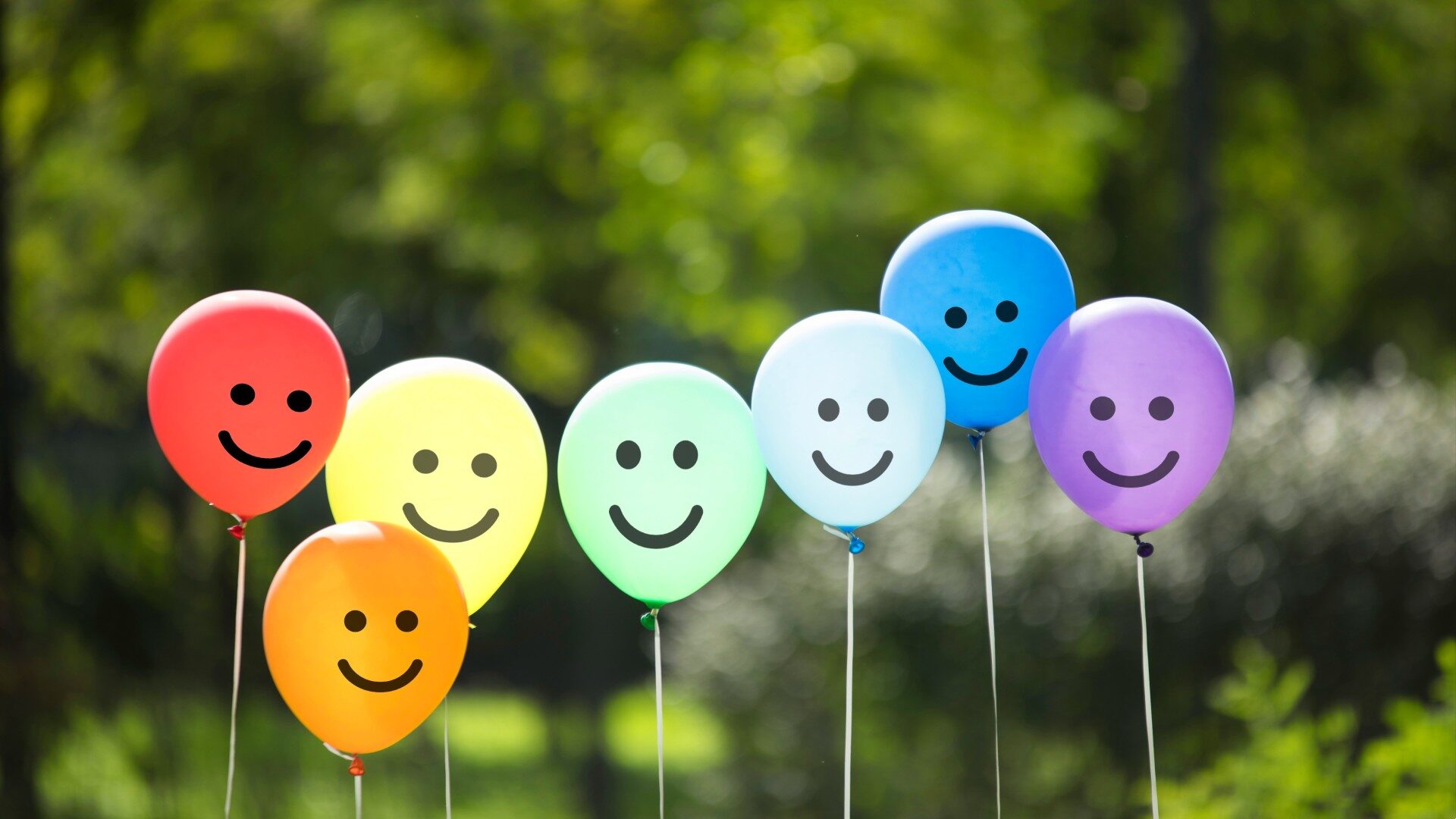 An assortment of balloons are pictured with smiley faces drawn on them