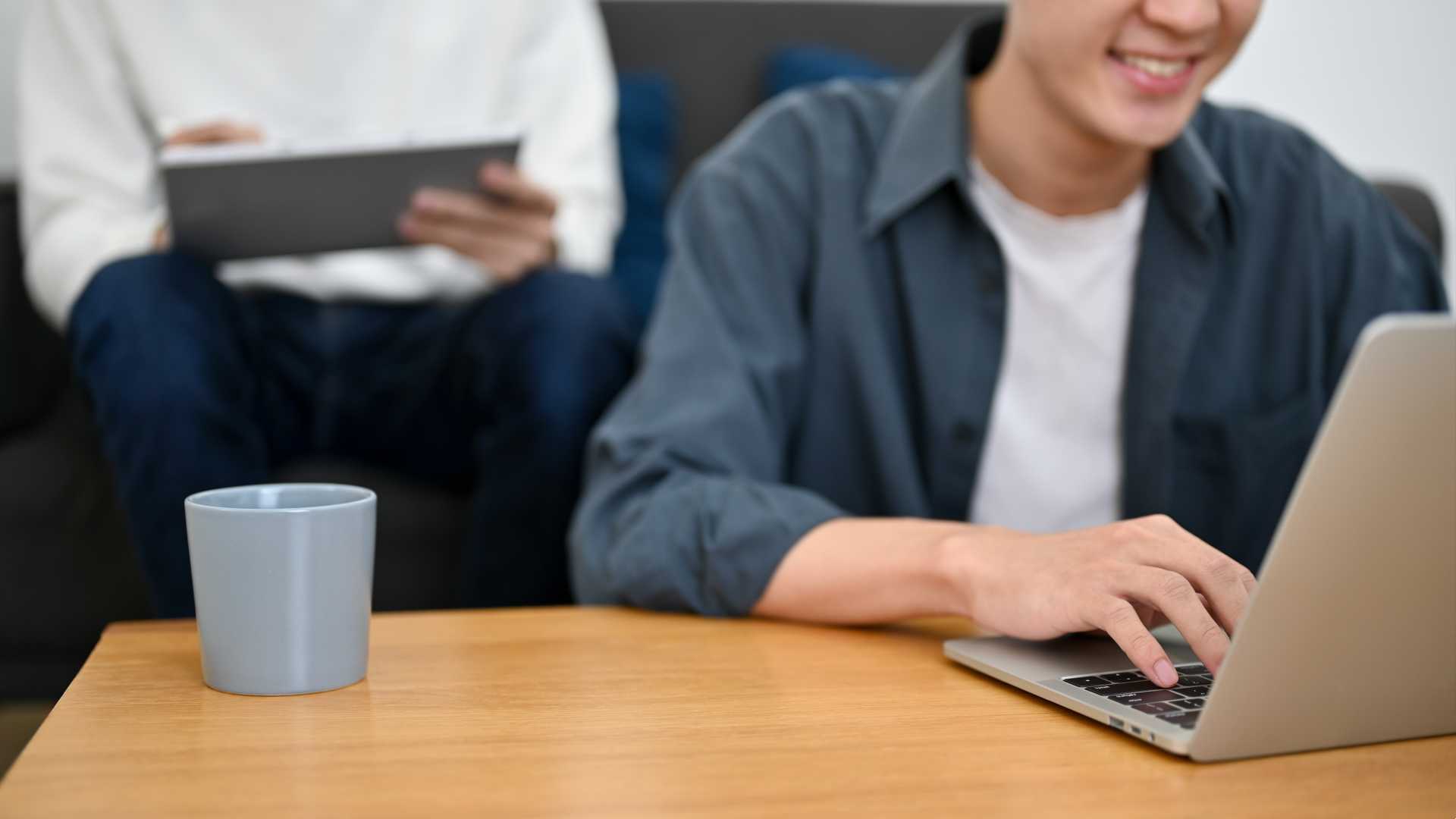 A male employee works on a laptop seated at a wooden desk