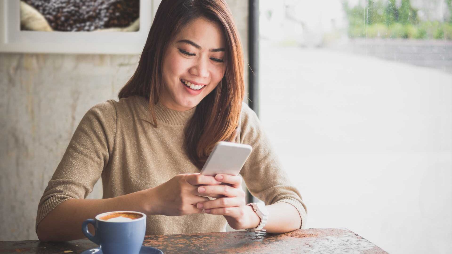 A young professional looks at her phone while seated in a coffee shop