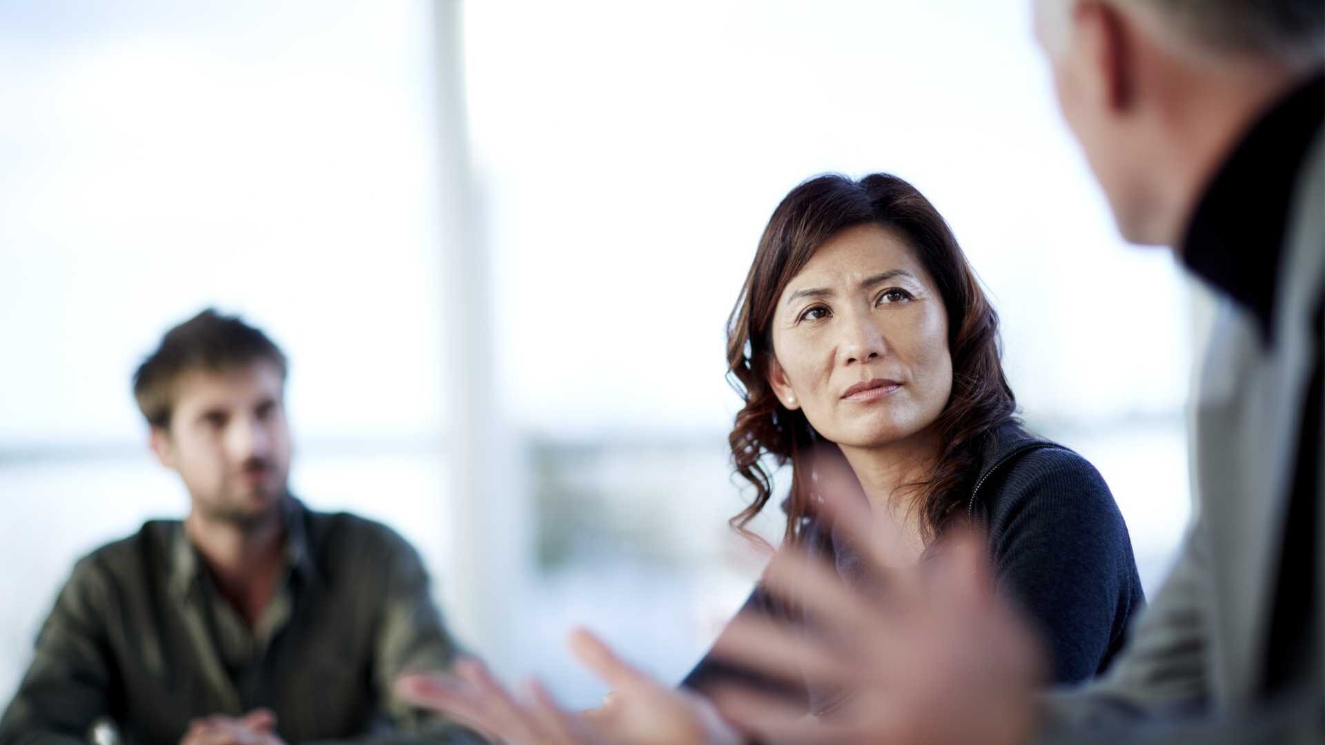 A woman and a man listen to a businessman speaking in a workplace setting