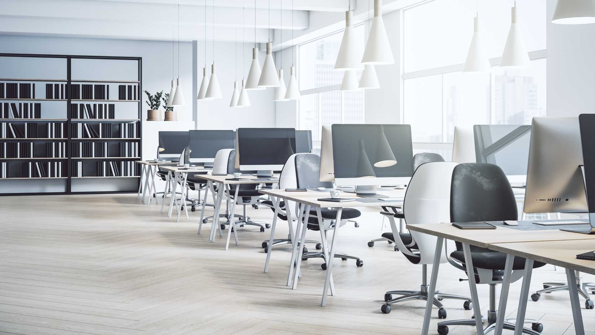 Empty office with computers on desks and a bookshelf in the background.