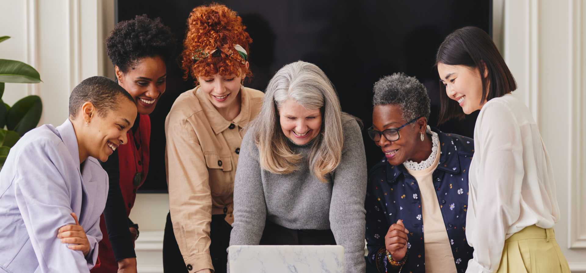 Group of women colleagues huddled together around a laptop.