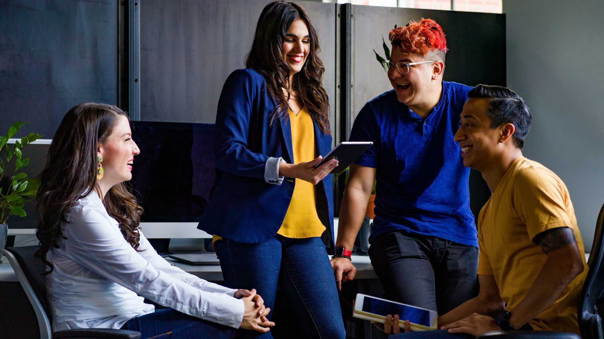 A group of people are laughing and talking in an office