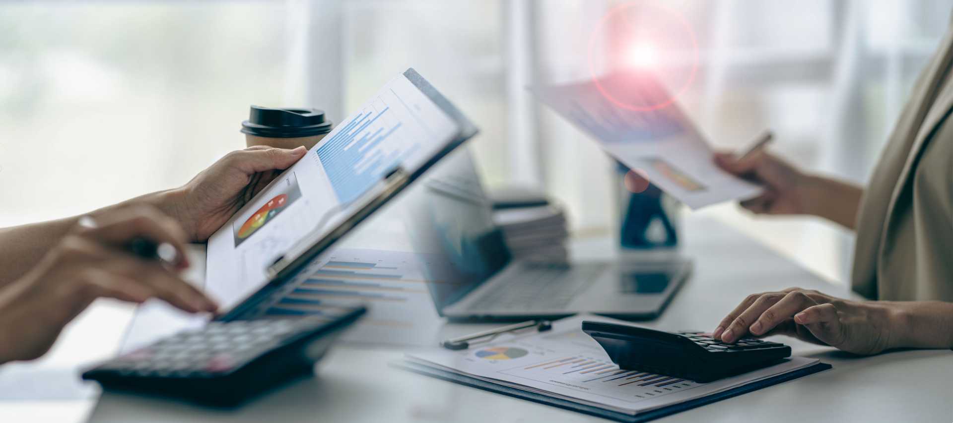 Papers outlining charts and graphs placed on a desk next to a laptop
