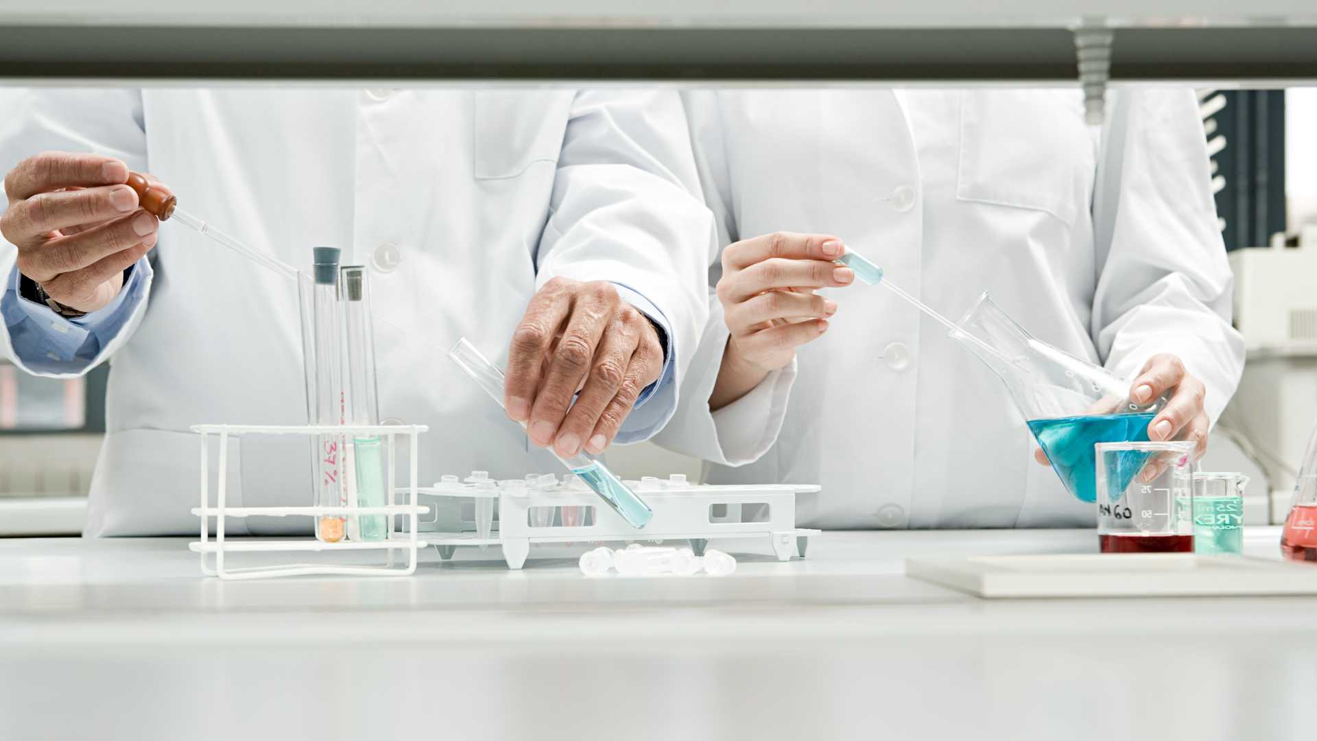 Close up photo of doctors in white lab coats working with beakers and test tubes.