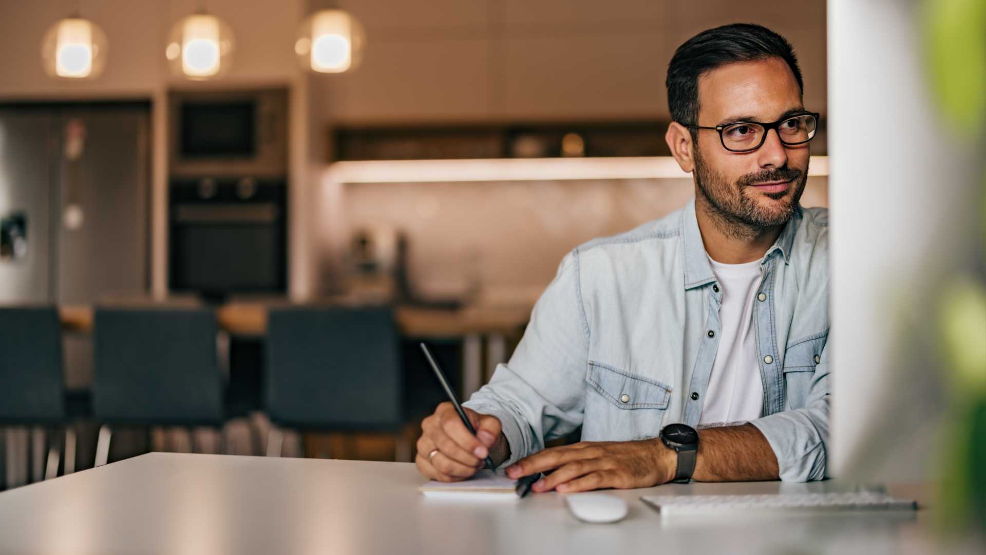 A person sits at a computer with a pen and paper in hand