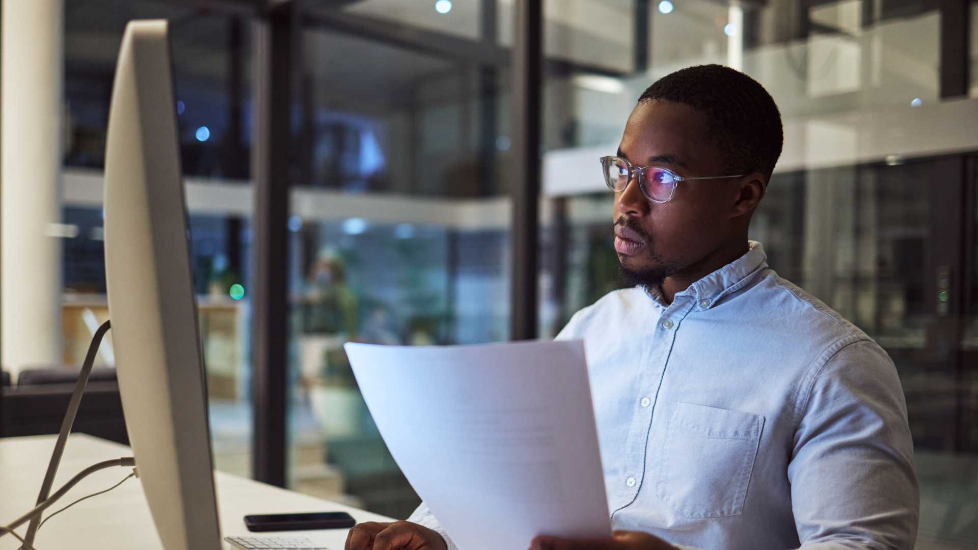 A young IT professional sits in front of his computer, reviewing a cloud skills training printout.
