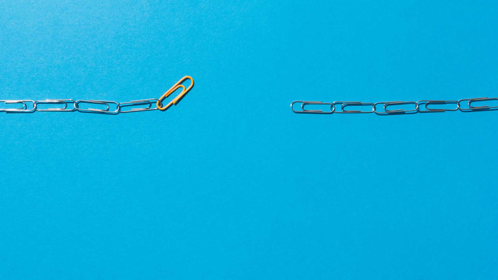 A broke line of paper clips with a yellow paper clip sticking up at the end of the left end.