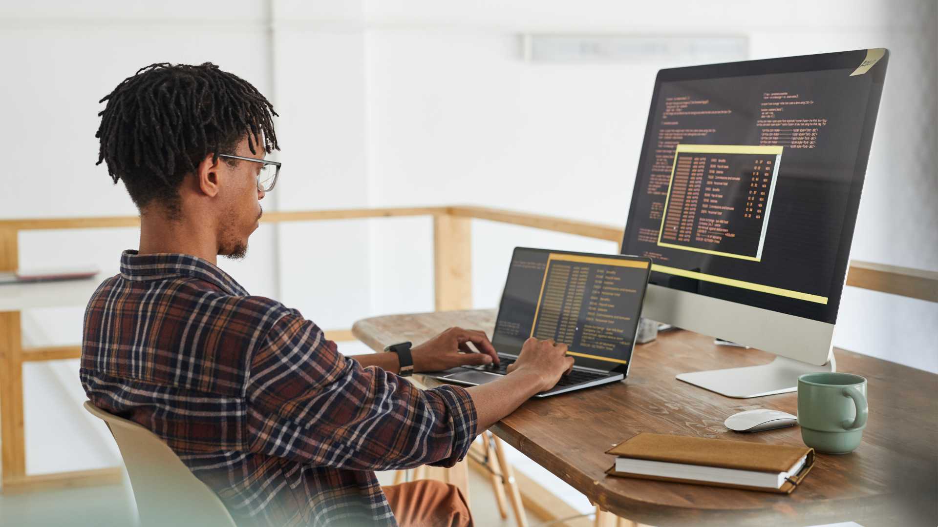 A young cybersecurity professional types on his laptop while looking at a second monitor.