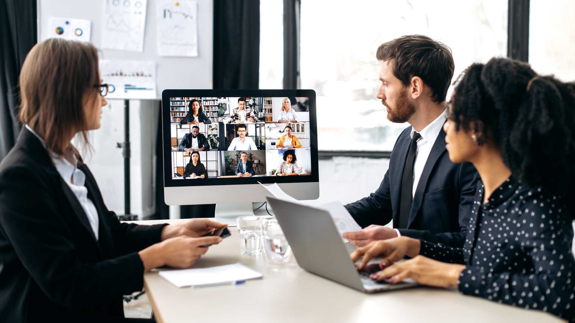 A hybrid business meeting takes place where employees chat with their virtual colleagues in a virtual meeting