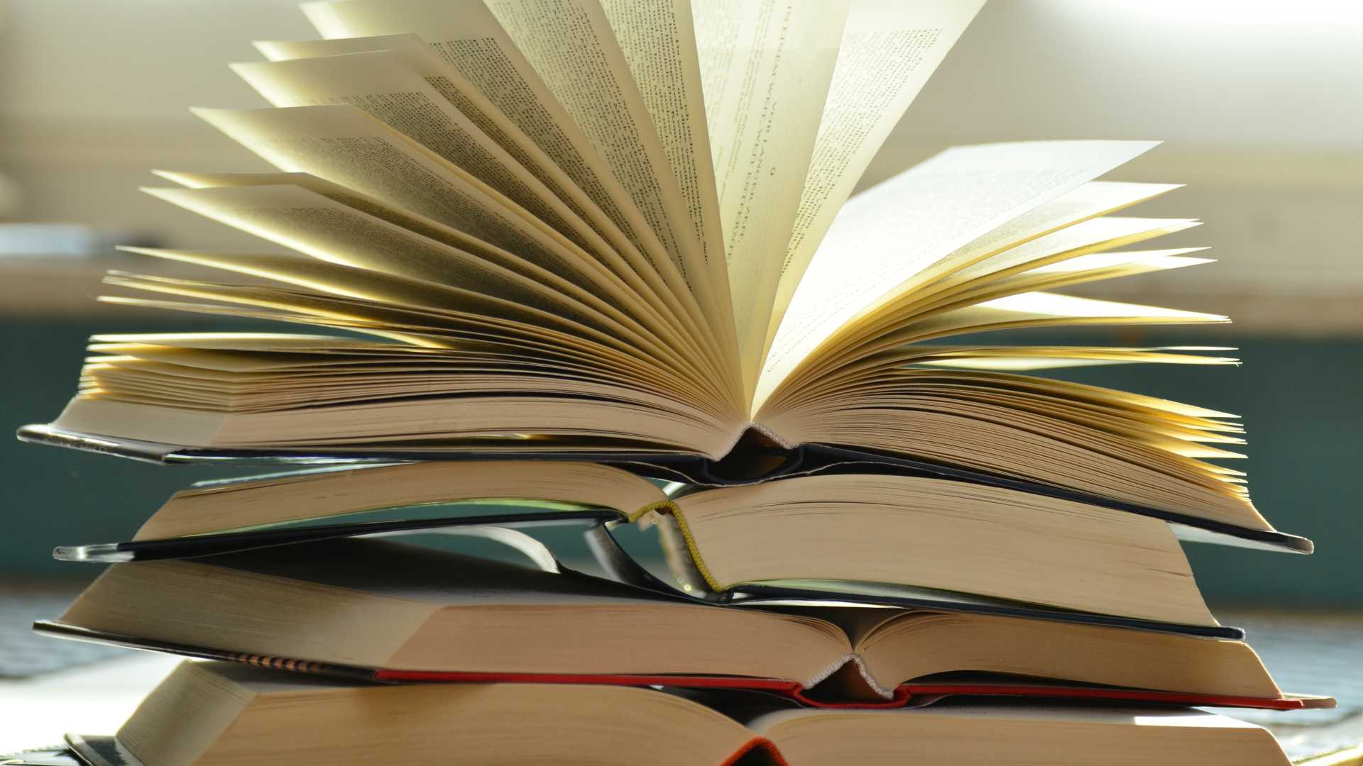A pile of books topped with an open book with its pages fanned out