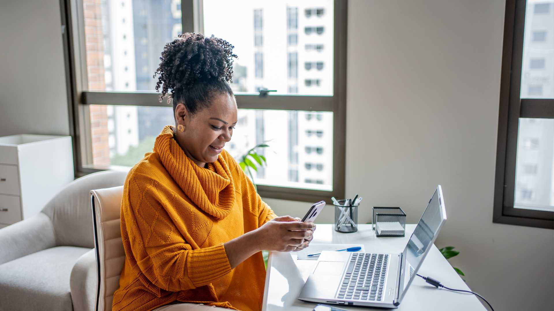 Person sitting at their at home office, with their phone, wearing a mustard yellow sweater