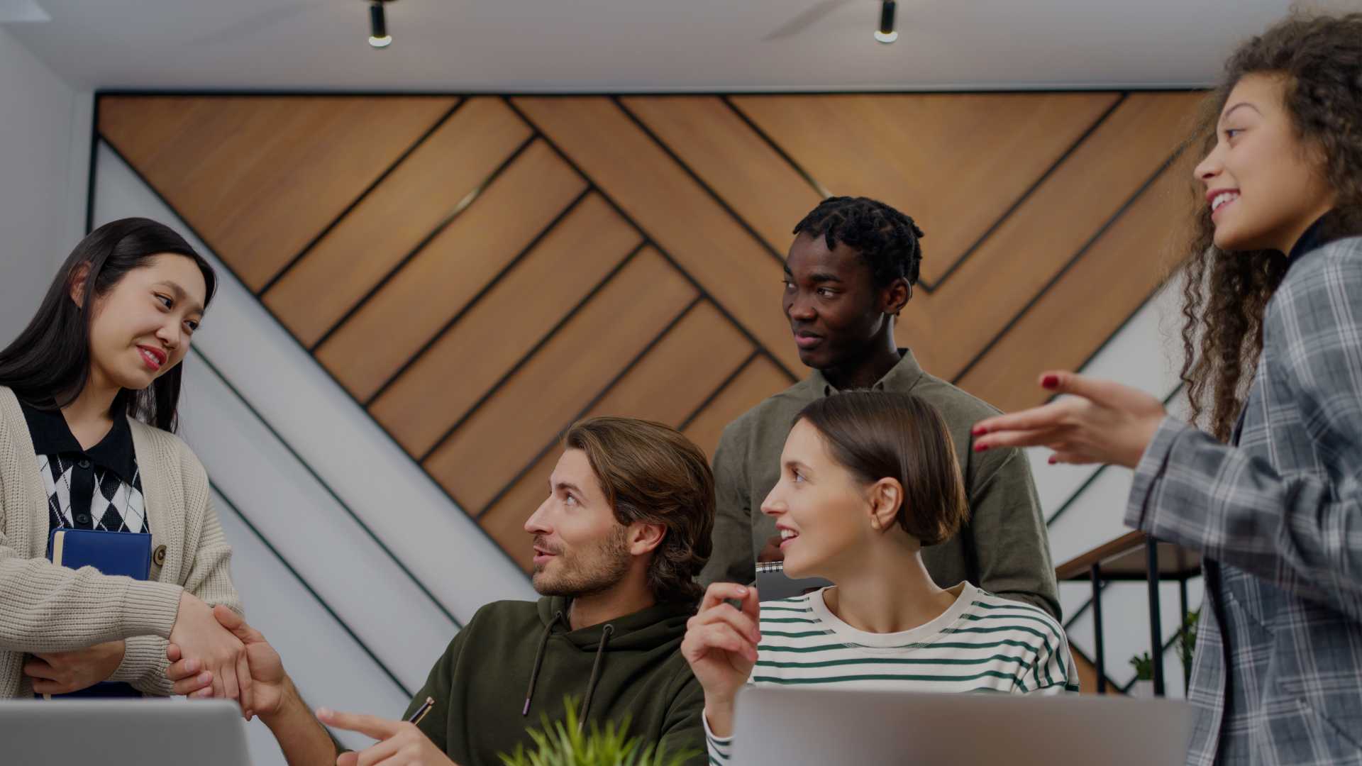 Team of colleagues greeting a new employee at a shared desk with laptops.