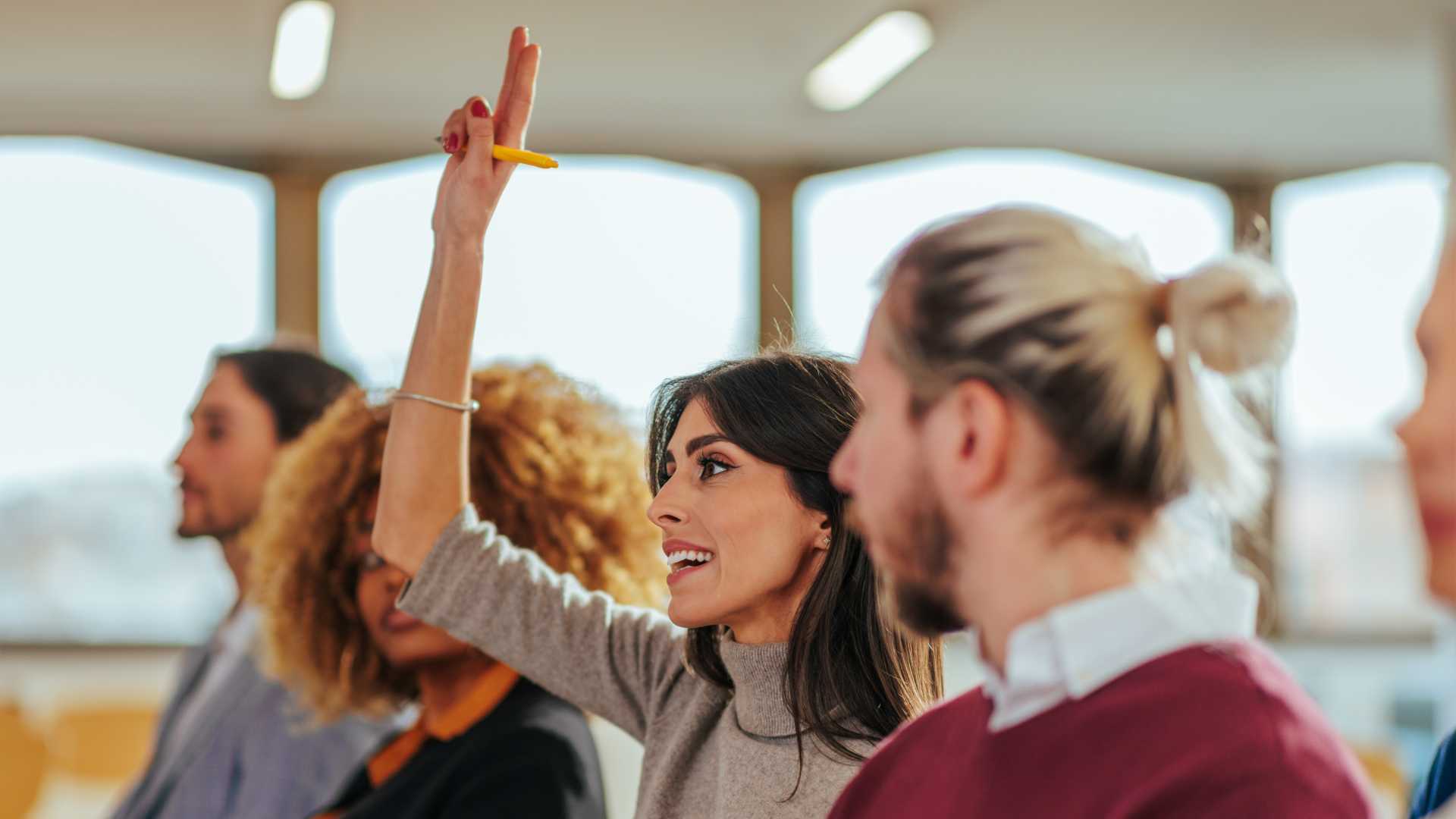 A young businesswoman in the audience of a tailored learning course raises her hand enthusiastically.