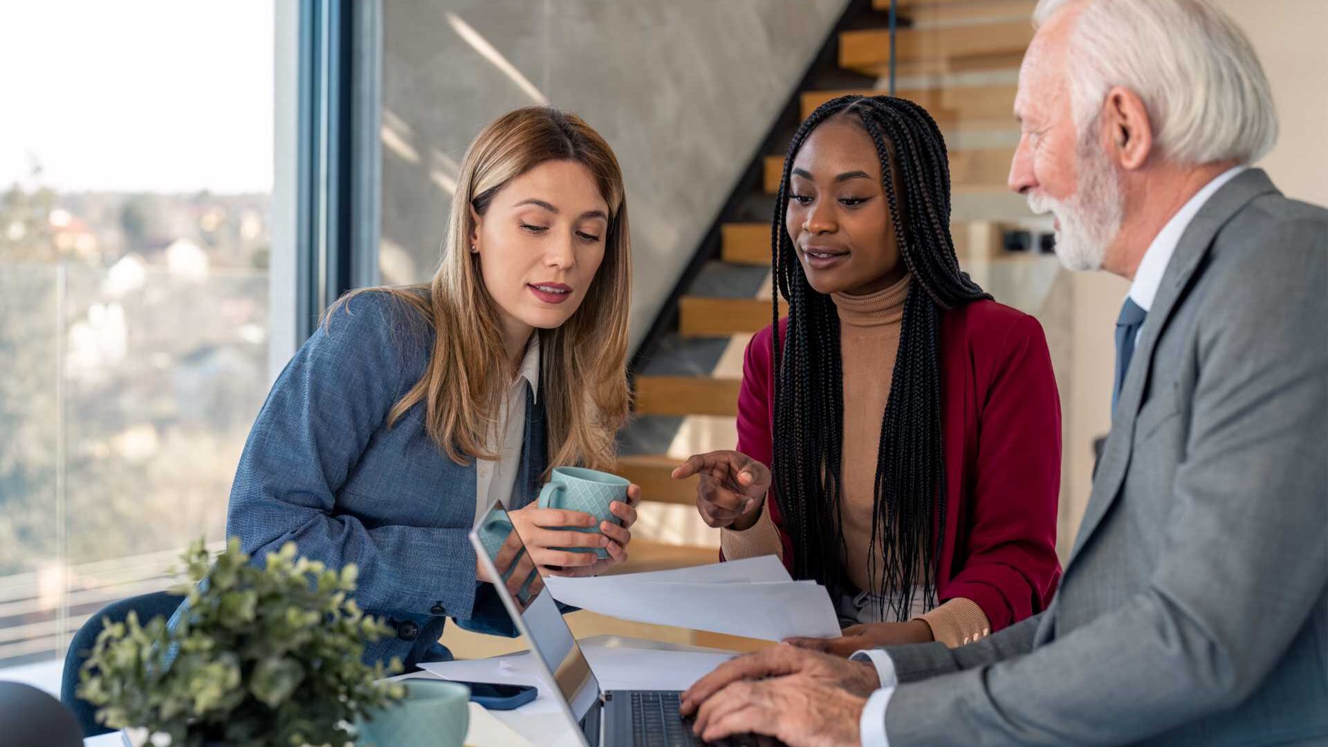 Three employees, one older man and two younger women, collaborate in an open office setting
