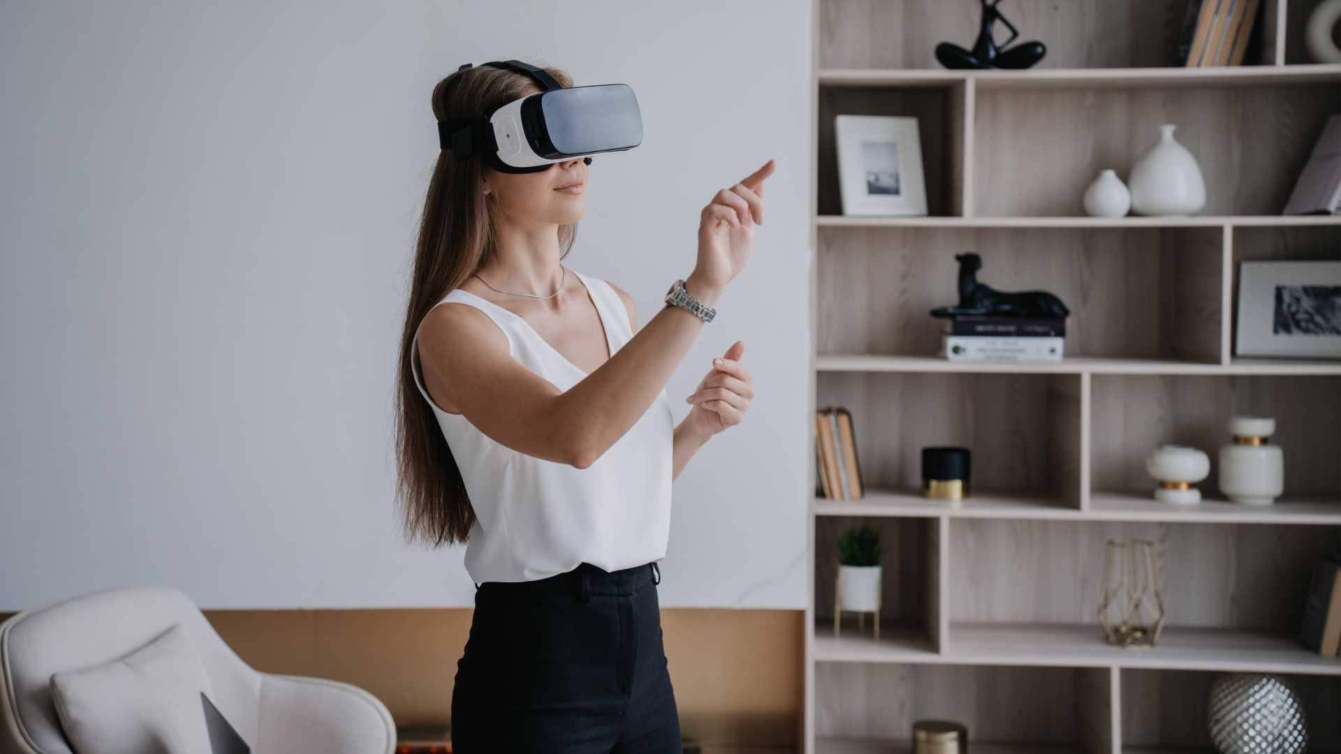 A woman working from home wears a virtual reality headset while pointing in the air