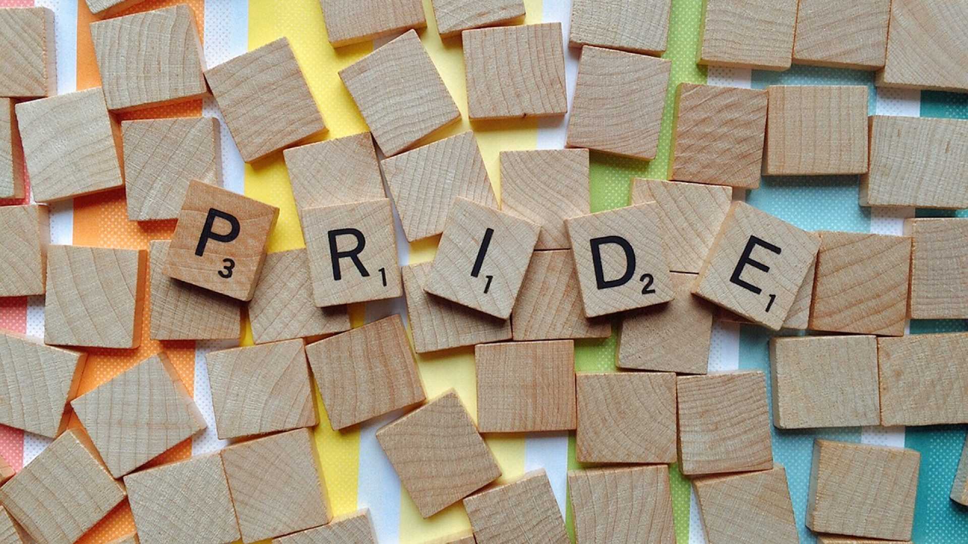 Scrabble pieces spell out the words PRIDE against a rainbow background